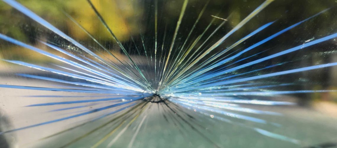 A close-up of a shattered windshield, showing the impact point and the cracks radiating outwards the car hit a butternut dropping out of a tree at 45 MPH